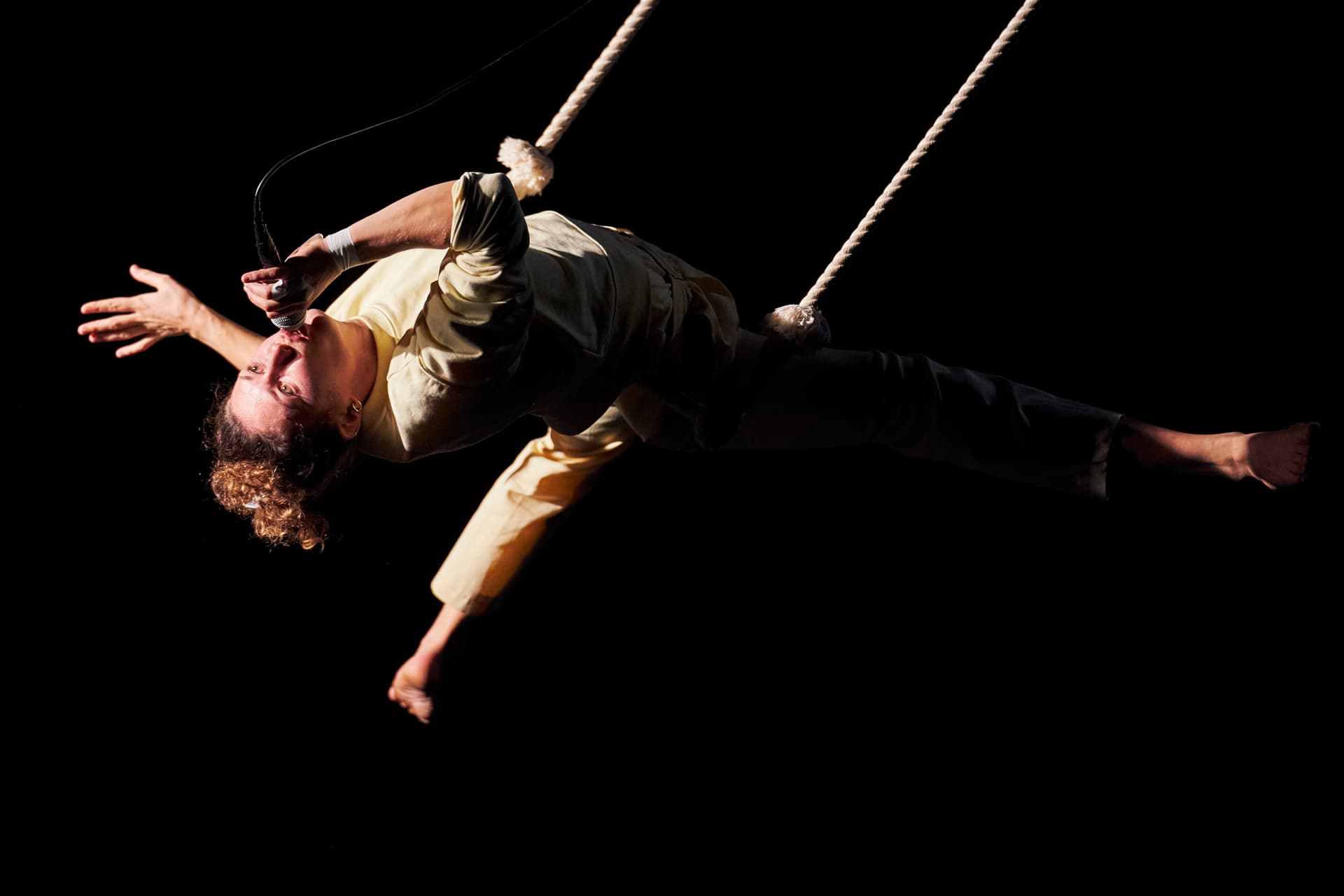 Eine Person mit einem Mikrofon am Mund hängt von einem Seil herab.